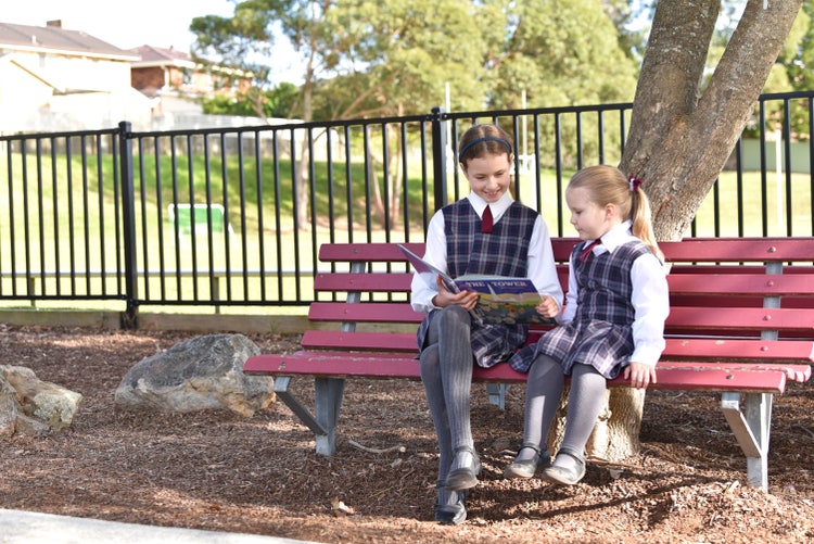 Two students sitting on a bench reading a book